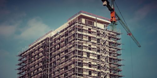 Upward angle on an apartment building complex under construction with a crane rising above it.