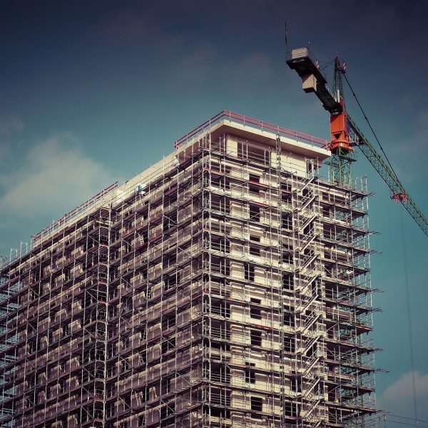 Upward angle on an apartment building complex under construction with a crane rising above it.