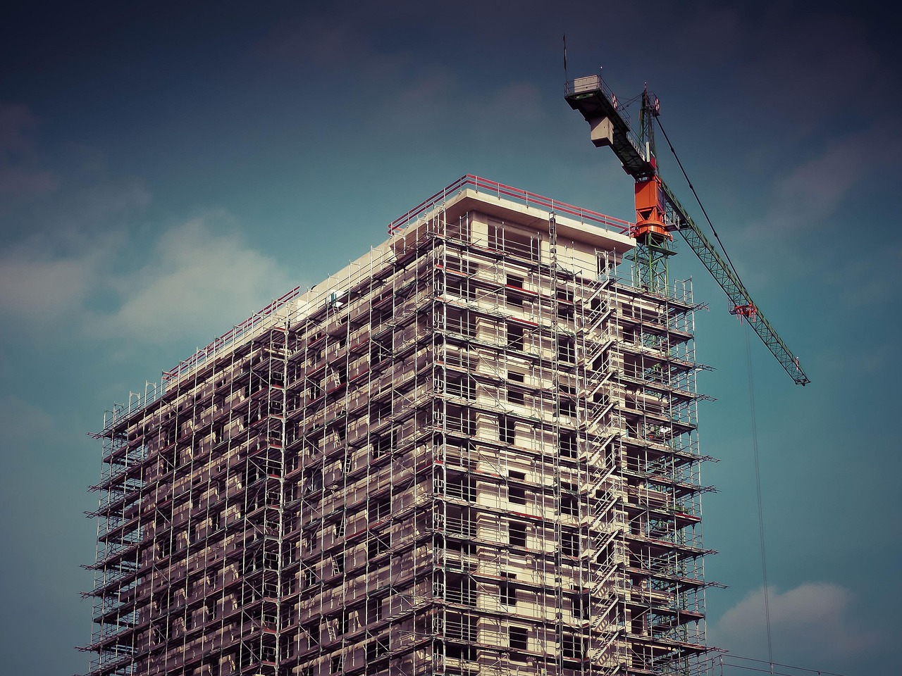 Upward angle on an apartment building complex under construction with a crane rising above it.